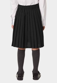 Falda negra plisada con cintura elástica, de tela ligera, combinada con calcetines oscuros hasta la rodilla y zapatos de charol negros.