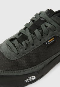 Mørkegrå sneakers med en blanding av teksturert svette og mesh, med svarte lisser, forsterket tå og merkevarelogo på siden.