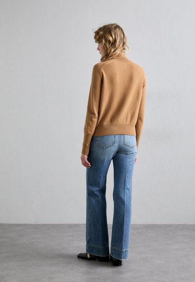 Barna kötött pulóver hosszú ujjakkal, magasan derékra szabott világoskék trapéznadrággal, mely nyers szegéllyel és diszkrét hátsó zsebfedéssel rendelkezik.