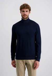 Marineblauwe coltrui van een gladde brei stof, met lange mouwen en een aansluitend ontwerp, gecombineerd met lichtgekleurde broek.