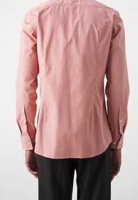 Lichtroze shirt met lange mouwen, met knoopsluiting bij de manchetten en een afgeronde zoom. Glad textuur met minimale kreuken en een klassiek pasvormontwerp.