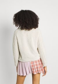 Pullover cremoso, morbido e con texture, con scollatura rotonda e maniche lunghe, abbinato a una gonna plissettata a quadri multicolori.