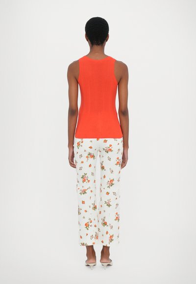 Rød ribbet tank topp kombinert med hvite blomstermønstrede vide bukser. Bukser har små rosa og oransje blomsterdesign.