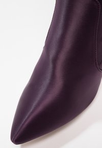 Zapato de satén púrpura con puntera afilada y textura suave. Sin hardware ni acentos visibles, centrándose en la forma refinada.