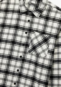 Schwarzes und weißes karotten Flanellhemd mit Knopfleiste, schwarzen Knöpfen und einer Brusttasche mit passendem Karomuster.