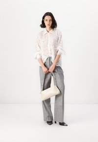 White sheer lace blouse with wave pattern, gray plaid high-waisted trousers, and a cream handbag. Model wears black shoes with pointed toes.