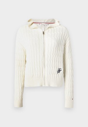 Cardigan zip-up a maglia intrecciata color crema con colletto alto e polsini a coste. Presenta un piccolo logo ricamato sul lato sinistro del petto e un dettaglio a righe all'interno.