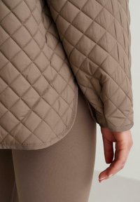 Brun quiltad jacka med en slät yta och rundad nederkant, ihop med matchande slim fit leggings i en liknande nyans.