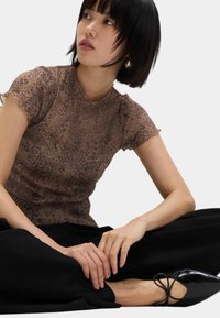 Genomskinlig brun topp med korta ärmar och leopardmönster, scalloped halsringning och lätt volangkant, kombinerad med svarta vida byxor och svarta skor.