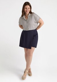 Blusa a maniche corte con bottone, caratterizzata da un motivo a fantasia, abbinata a una gonna blu navy con un taglio diagonale e dettagli in cucitura rossa.