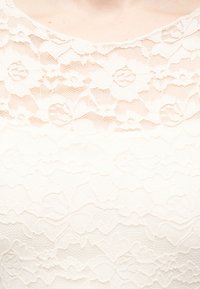 Κοντινό σε λευκή δαντελένια μπλούζα με λουλουδάτα σχέδια που καλύπτουν το πάνω μέρος του στήθους και την περιοχή του λαιμού.