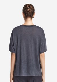 Grå, kortärmad t-shirt gjord av lättviktsmaterial, med en avslappnad passform och en subtil textur. Bakifrån syns en rundad halsringning.