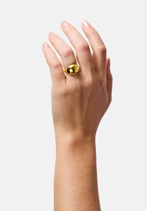 Gold ring, teardrop shape with a smooth, reflective surface. Worn on a hand with natural nails against a plain background.