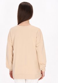 Beige sweatshirt s dlouhým rukávem a uvolněným střihem, kulatým výstřihem, širokými manžetami a hladkým povrchem. Bez viditelných vzorů nebo grafik.