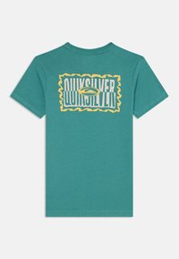 Tirkīza t-krekls ar izteiksmīgu dzeltenu un baltu Quiksilver logo ar viļņveida malu. Izgatavots no mīksta kokvilnas auduma, ar īsām piedurknēm un apaļu kakla izgriezumu.
