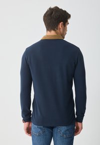 Marineblå langermet polo-skjorte med en kontrastfarge i brun på kragen, laget av bomull, med en glatt tekstur og en avslappet passform.