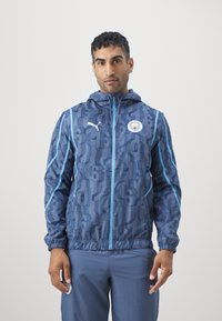 Giacca con cappuccio azul navy con un motivo testurizzato che presenta numeri, accenti blu chiaro e il logo Puma. Maniche elastiche e chiusura con zip.