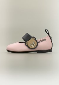 Chaussure plate rose pour enfant avec une bride noire ornée d'un patch ours en peluche et du logo Moschino sur le côté et la languette du talon.