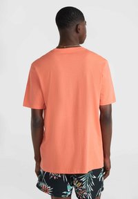 Camiseta de manga corta en color coral, fabricada con algodón suave. Presenta un escote redondeado y un diseño holgado, combinada con pantalones cortos estampados.