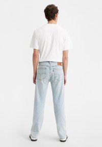 Ljusblå denimjeans med rak passform, med bakfickor och en läderlogotyp. Bärs med en vit t-shirt.