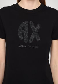 Černé bavlněné tričko s lesklým černým logem "AX" a textem "ARMANI EXCHANGE" pod ním v elegantním písmu. Kulatý výstřih.