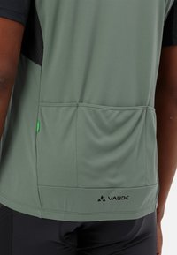 Szaro-zielona koszulka sportowa z czarną siateczkową wstawką, z tylną kieszenią i logo Vaude na dolnym brzegiem, wykonana z gładkiego, elastycznego materiału.