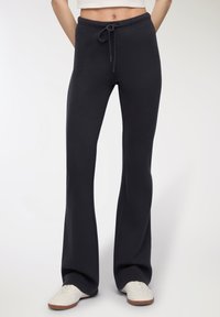 Czarne dzwony ze swobodnymi spodniami z miękkiego materiału, z elastycznym paskiem w talii i regulowanym sznurkiem, charakteryzujące się luźnym krojem aż do kostek.