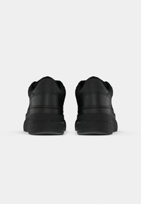 Paire de baskets noires vues de dos avec des semelles épaisses et "Tommy Jeans" embossé sur la zone du talon.