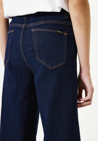 Donkerblauwe denim wijd uitlopende jeans met oranje stiksels. Vier zakken, met het label "GARCIA" op de achterkant. Gladde textuur, klassiek ontwerp.