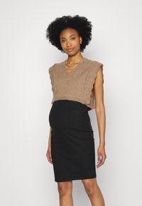 Pull castanho curto com decote em V e bordas onduladas, combinado com um vestido de maternidade preto em riscas que se ajusta à silhueta.