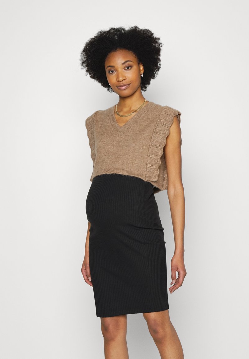 Pull castanho curto com decote em V e bordas onduladas, combinado com um vestido de maternidade preto em riscas que se ajusta à silhueta.