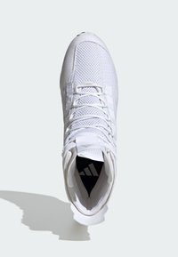 Zapatilla deportiva blanca con parte superior de malla texturizada, cierre de cordones y collar acolchado. Presenta una plantilla negra con un logo y una suela lisa.