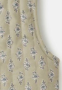 Tan tyg med ett blommönster i blått och vitt. Sattentextur med subtila sömdetaljer, formad med en rundad halsringning och sidöppningar.