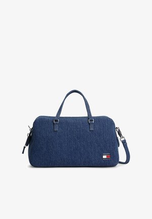 Sac à main en denim bleu avec deux poignées supérieures, une bandoulière amovible et un petit logo rectangulaire sur la partie inférieure avant droite.