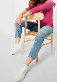 Pink long-sleeve shirt with white stripes at cuffs, blue denim jeans, and white sneakers on a wooden chair. Casual outfit with relaxed fit.