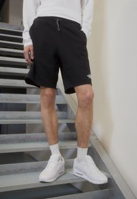 Shorts en coton noir avec une taille élastique et un cordon de serrage, associés à des baskets montantes blanches et des chaussettes côtelées, sur des escaliers en métal.