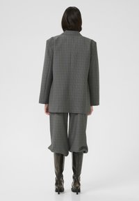 Grau karierter Blazer mit lockerer Passform, kombiniert mit weiten Hosen und knielangen schwarzen Stiefeln, die einen maßgeschneiderten, aber lässigen Look zeigen.
