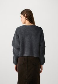 Γκρι υφασμάτινος πουλόβερ με φαρδιά γραμμή και μακριά μανίκια, συνδυασμένο με μια σκούρα καφέ φούστα που διαθέτει πίσω τσέπες και κατακόρυφες ραφές.