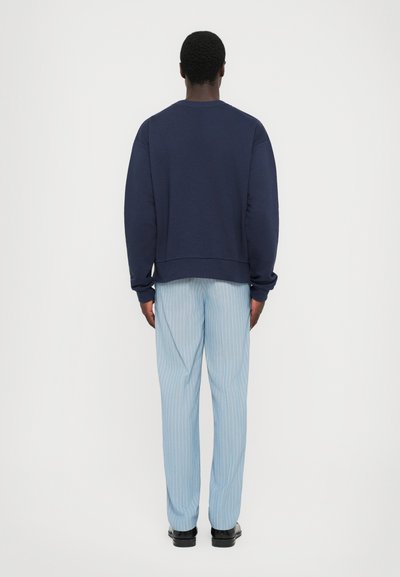 Felpa girocollo blu navy con maniche lunghe abbinata a pantaloni a righe sottili blu chiaro e scarpe nere, vista da dietro.