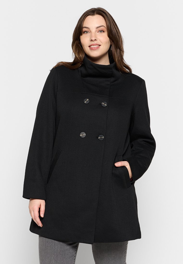 Cappotto in misto lana nero con colletto alto, bottoni doppi e tasche laterali. Presenta una forma classica e strutturata con una texture liscia.