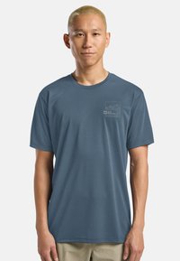 Maglietta a maniche corte da uomo in tessuto blu. Collo rotondo, morbido al tatto, con una sottile grafica di montagne sul petto sinistro.