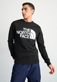 Sudadera negra hecha de una mezcla de algodón, con un gran logo blanco en la parte frontal. Cuello y puños acanalados, corte relajado y diseño simple.