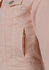 Giacca di denim rosa con finitura testurizzata, tasca frontale con patta e dettagli di cucitura visibili. Chiusura a bottone nella zona del colletto.