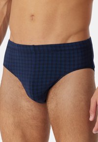 Männlicher Oberkörper, der navyblaue Unterhosen mit hellblauem Karomuster trägt, sichtbar sind der Unterbauch und die Oberschenkel.