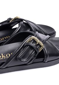 Zwarte leren sandalen met kruislings gespen, voorzien van een gouden gesp detail. Geverfde voetbed en platte rubbersole voor comfort.