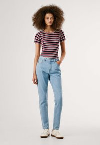 Top de manga corta a rayas en negro, rojo y blanco con pantalones vaqueros de tiro alto en azul denim. Los zapatos son blancos con suelas de marrón claro. Textura suave.