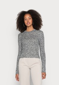 Camisa de manga longa cinza com design de malha texturizada, gola redonda e silhueta ajustada. Combinada com calças de cor clara.