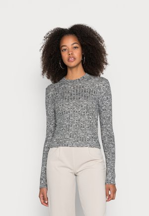 Camisa de manga longa cinza com design de malha texturizada, gola redonda e silhueta ajustada. Combinada com calças de cor clara.