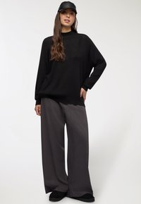Maglione nero oversize con maniche lunghe, abbinato a pantaloni larghi e morbidi grigio scuro e scarpe slip-on nere. Berretto in pelle nera.