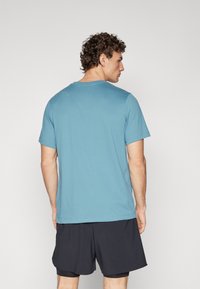Short-sleeve teal t-shirt made of cotton, featuring a crew neck and a relaxed fit, paired with dark shorts.
